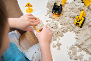 The child engages in a sensory activity, feeling the soft kinetic sand under their hands. Kid aged...