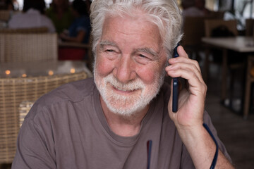 Close up portrait of senior bearded man sitting in a cafe shop smiling while using mobile phone. Elderly male using modern technology for online connection