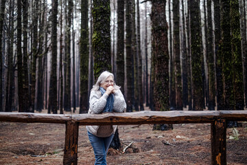 Smiling mature woman resting in mountain forest on a winter foggy day enjoying nature, freedom and free time. Bare trees on backgrounds