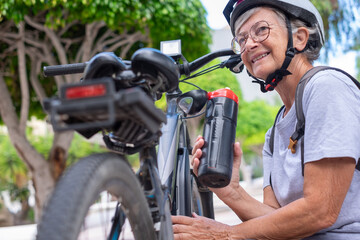 Fototapeta premium Smiling senior caucasian cyclist woman in leisure activity in urban park riding with electric bike enjoying healthy lifestyle
