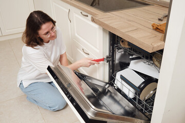 Woman repairing a dishwasher with a wrench in a modern kitchen. Home appliance maintenance and kitchen repair concept.