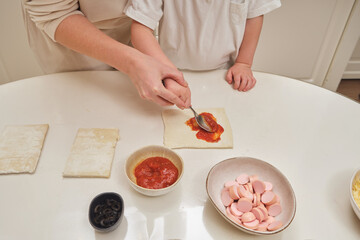 In a cheerful kitchen scene, a mom and her child are baking a homemade pie. A family moment in the kitchen shows a mother and her toddler making pizza from scratch.
