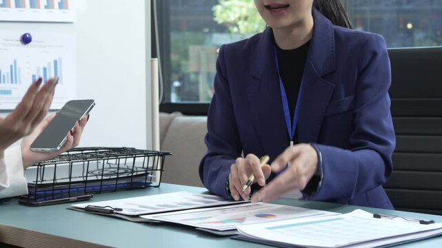 Two Asian female business woman sit desk,discussing business investments.They analyze financial data, explore market opportunities, and strategic growth to maximize returns ensure business success