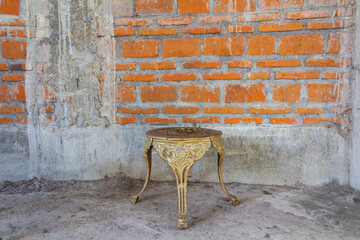 Vintage Brass Table or Chair on Rough Textured Concrete Floor with Red Brick Wall Constructions.