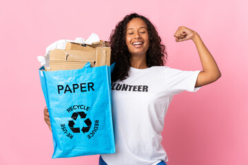 Teenager cuban girl holding a recycling bag full of paper to recycle isolated on pink background...