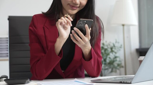 A young businesswoman works at her desk in an office, talking on the phone while using a computer. She plans strategies, analyzes data, and manages tasks to drive business success