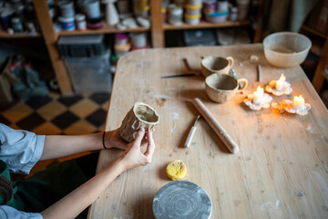 Unrecognizable woman potter mold clay cups with intricate pattern on wooden table in workshop. Handmade ceramics, artisan craft, creative artistry, small business, artisan school, crockery product