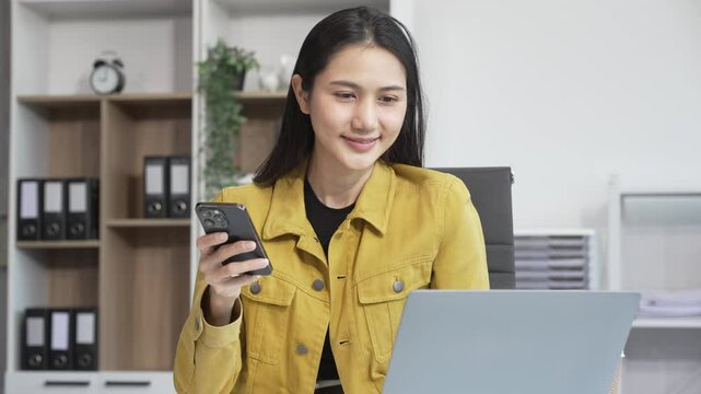 A young businesswoman works at her desk in an office, talking on the phone while using a computer. She plans strategies, analyzes data, and manages tasks to drive business success