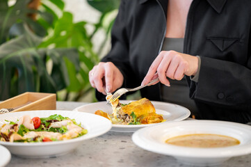 A close-up of a hand holding a fork and knife, preparing to enjoy a delicious meal. In the background, plates of salad and soup are artfully arranged, enhancing the vibrant dining experience.