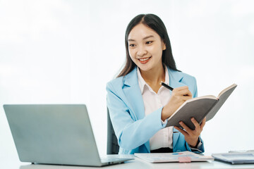 An Asian female accountant works happily at her desk in the office, using a laptop to analyze financial charts. She manages business finance and online transactions for company success