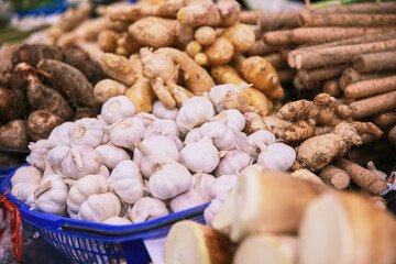 A basket of garlic and other vegetables are displayed in a market. The garlic is white and the vegetables are green