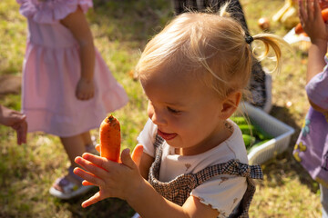 Naklejka premium Little girl enjoying a carrot during a fun outdoor gathering on a sunny day