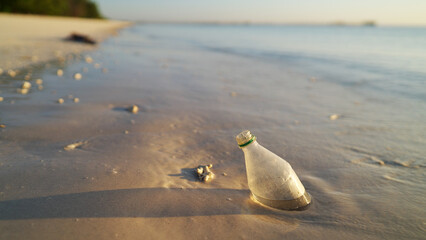 Single plastic bottle stuck in sand on beach at sunset highlighting marine pollution. Concept of...