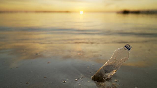 Plastic water bottle on sandy beach at sunset, ocean in background, marine pollution problem, discarded waste on coastal ecosystems