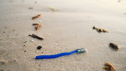 A discarded toothbrush on a beach with sea in background, plastic waste in nature