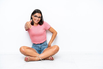 Fototapeta premium Young caucasian woman sitting on the floor isolated on white background shaking hands for closing a good deal
