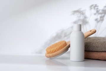 Skincare bottle, wooden body brush, and towels on a white surface