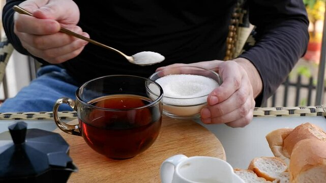 Male hands adding sugar into big cup of tea on table