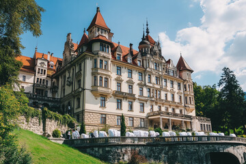 Fototapeta premium Historic mansion with intricate architecture, surrounded by lush greenery and blue skies, representing grandeur, elegance, and old-world charm in a picturesque setting.