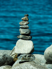stack of stones balancing in a pile on a rock in front of the ocean. The rocks are smooth and a tranquil form of art in nature