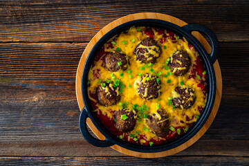 Cowboy meatballs baked with cheddar cheese in frying pan on wooden table