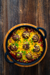 Cowboy meatballs baked with cheddar cheese in frying pan on wooden table