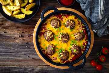 Cowboy meatballs baked with cheddar cheese in frying pan on wooden table