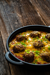 Cowboy meatballs baked with cheddar cheese in frying pan on wooden table
