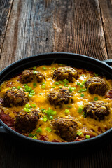 Cowboy meatballs baked with cheddar cheese in frying pan on wooden table