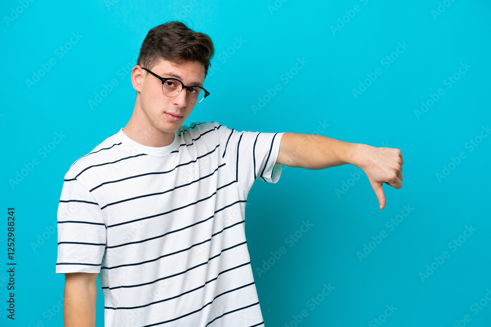 Wall mural Young handsome Brazilian man isolated on blue background showing thumb down with negative expression