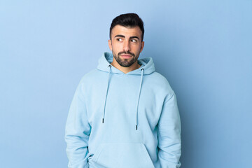 Caucasian man over isolated blue background having doubts while looking side