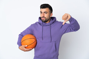 Man playing basketball over isolated white wall showing thumb down with negative expression