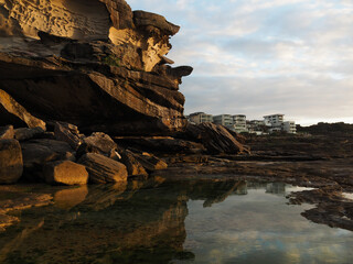 sunrise glow along the rocks of tamarama beach in sydney, australia, with the reflection of rocks in a rock pool