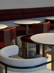 The cafe interior boasts elegant round tables and stylish velvet chairs in burgundy and light shades. A modern minimalist design creates a warm and inviting atmosphere.