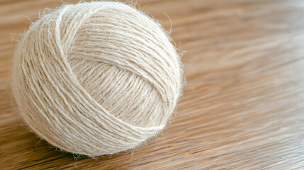 Fototapeta premium Single ball of natural beige wool yarn resting on a rustic wooden table in soft daylight.