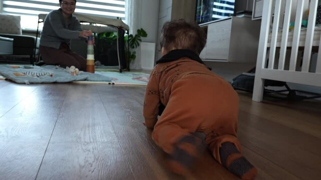 Little baby boy playfully crawling towards his mother in the living room.