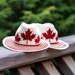 A close-up of a pair of red and white hats with maple leaf designs, resting on a wooden railing with a Canadian flag in the background, celebrating Canada Day.