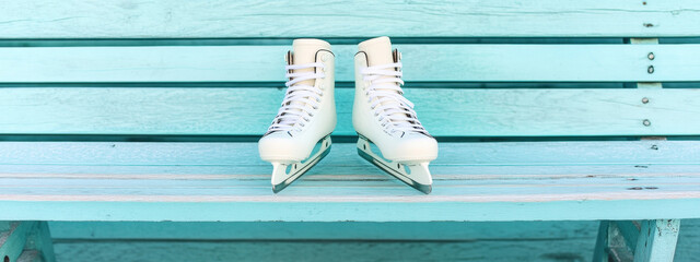 A pair of white ice skates resting on a pastel blue wooden bench, evoking a sense of calm and anticipation before an ice skating adventure.