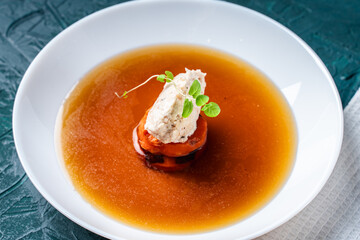 Soup or consomme, thick meat broth with carrots, chicken dumplings and microgreens, served in a white plate on a dark green background.