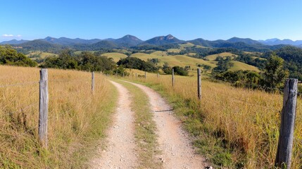 Naklejka premium Countryside Dirt Road Leading to Hills, Sunny Day, Rural Landscape, Perfect for Travel Brochure or Nature Photography