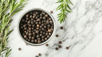 Metal cup overflowing with black peppercorns, placed next to sprigs of rosemary on a marble countertop