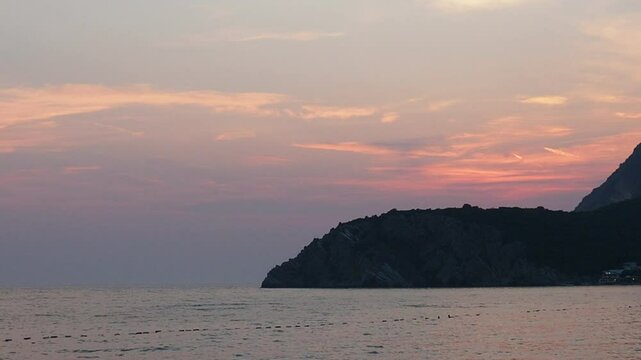 Witness the breathtaking view of a calming sunset at a coastal location. The horizon blends warm colors while waves gently lap at the shore. A peaceful moment in nature unfolds. Canj, Montenegro