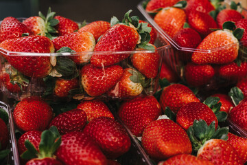 Clear plastic containers of fresh berries with the stems still on them. The packages are stacked on top of each other on a local market. The berries are firm, rich, and vibrant.