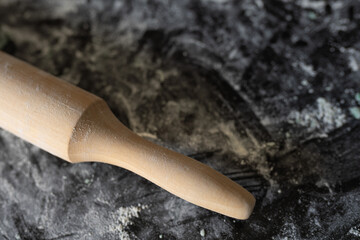 Close-up of a rolling pin surrounded by scattered flour on a black textured surface, evoking the...