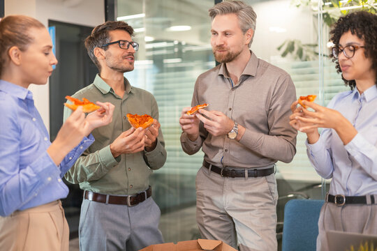 Happy multiracial colleagues have fun at lunch break in office. Excited workers celebrate shared win ordering takeaway pizza