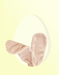 Cute festive bunny or rabbit toy ears hatching from a hole in shape of hen egg or hiding inside eggshell cut out on light yellow background used as a surprise greeting gift for easter holiday party
