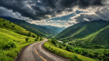 Fototapeta premium A winding mountain road through lush green valleys under a dramatic cloudy sky.