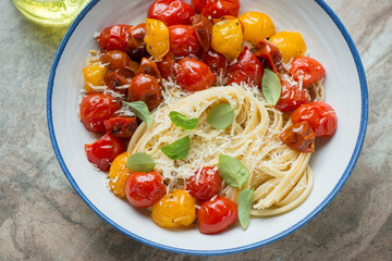 Linguine with roasted cherry tomatoes, grated cheese and basil served in a white and blue plate, horizontal shot, middle closeup