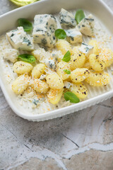 Potato gnocchi served with blue cheese and green basil, vertical shot on a grey granite background, middle close-up