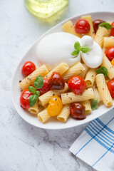 Tortiglioni pasta with roasted cherry tomatoes and burrata cheese, vertical shot on a white stone background, middle close-up